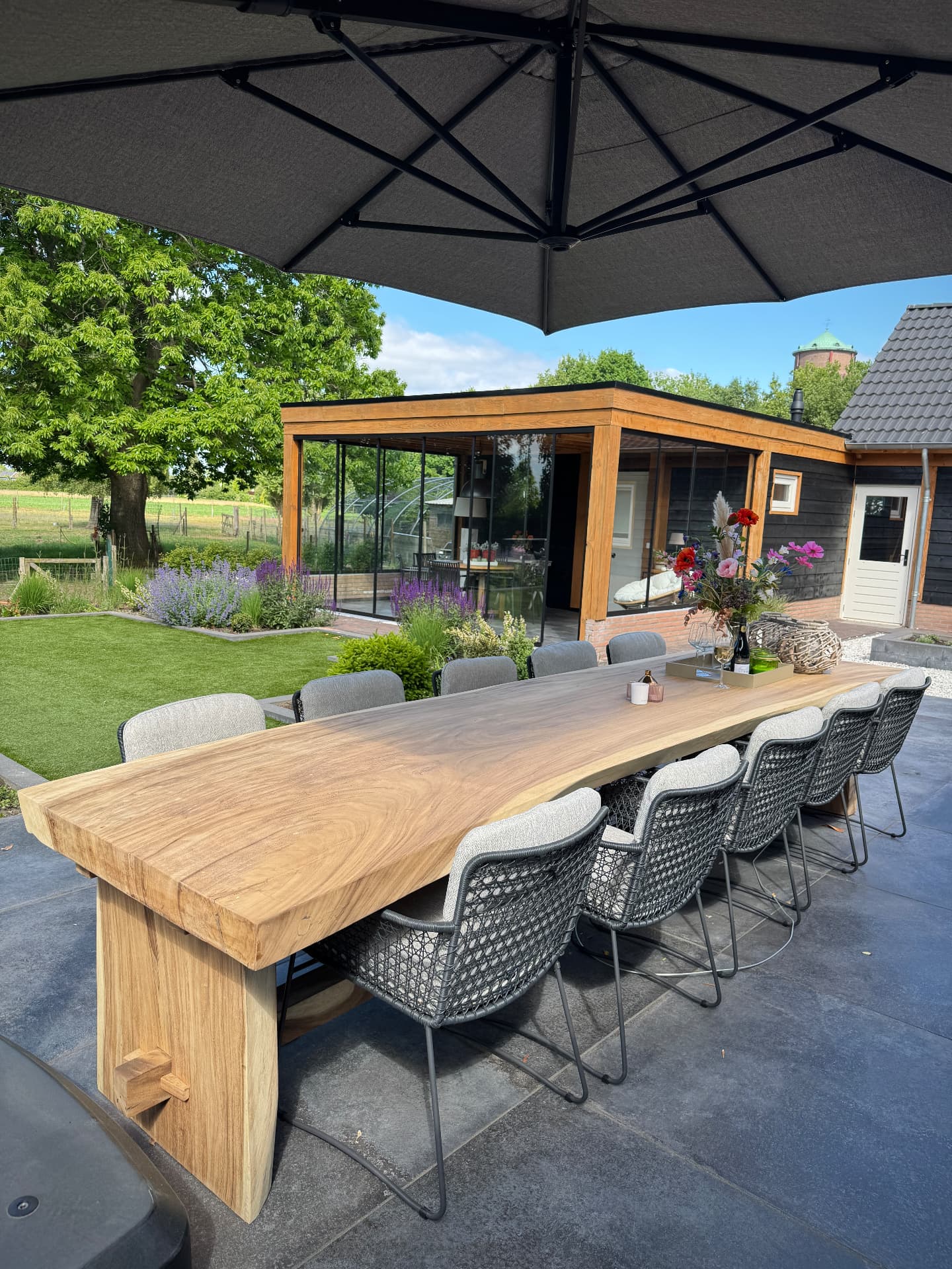 Huisje voor 11 personen: lange buitentafel met stoelen onder de parasol